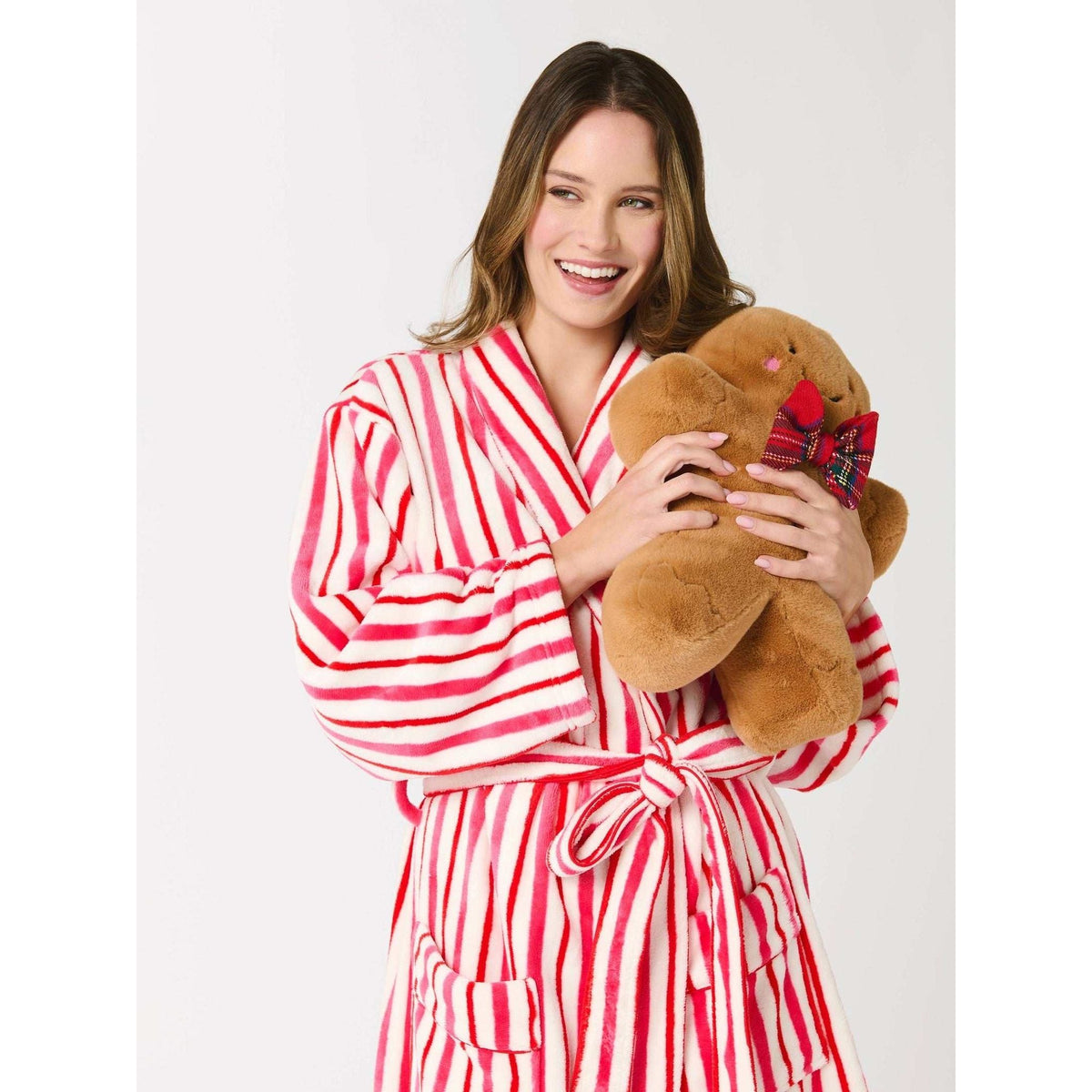 
                  
                    Woman in red and white striped robe holding a plush Gingerbread Man Pillow with tartan bowtie and stitched details
                  
                