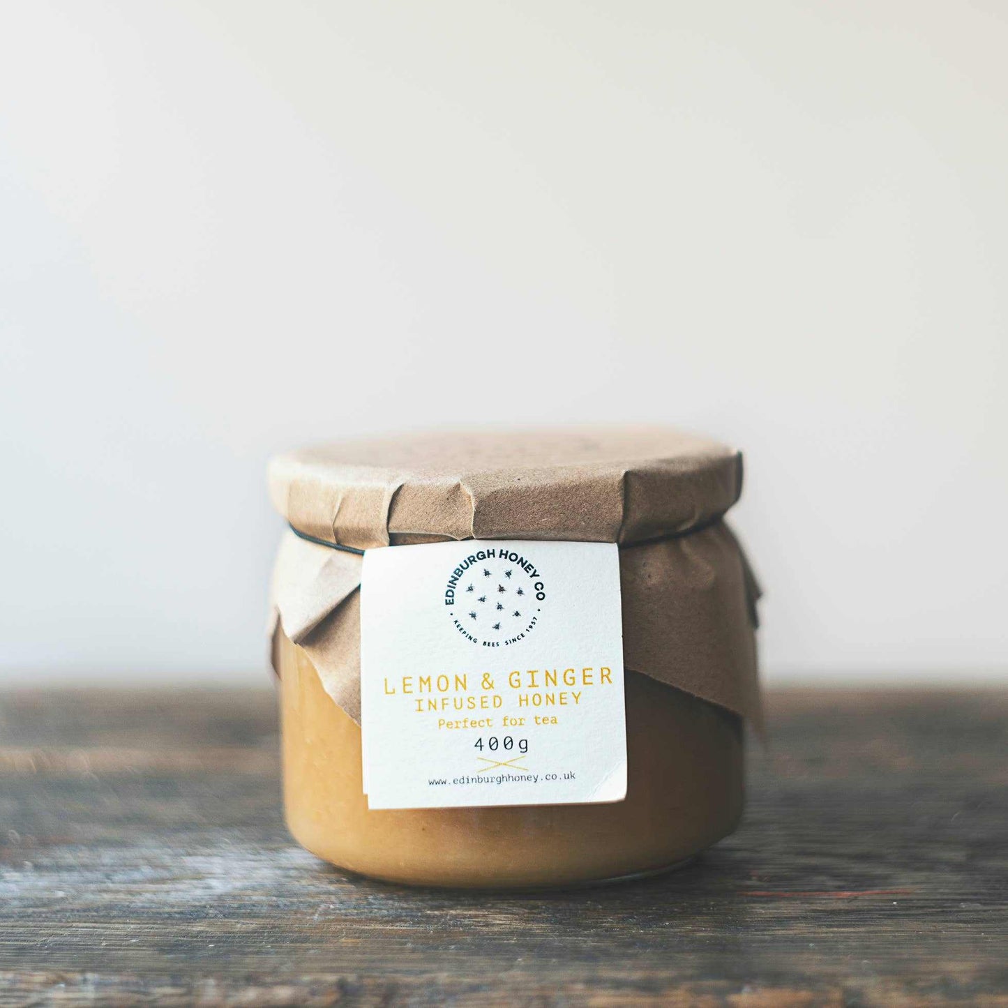 Jar of Edinburgh Honey Co. Lemon & Ginger Infused Honey 400g with paper cover on wooden surface