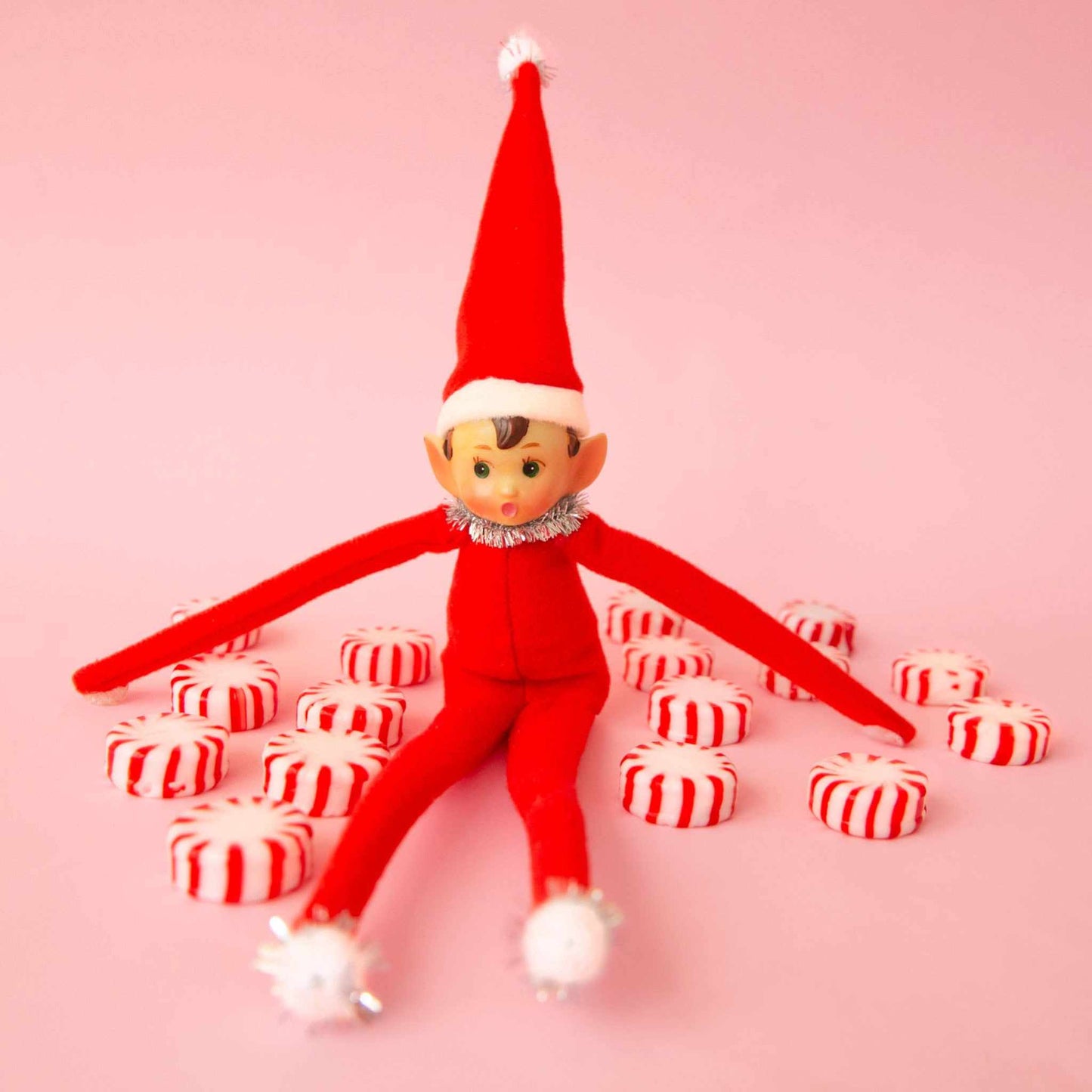 Festive Frankie elf ornament with bendable limbs and tinsel collar sitting among peppermint candies