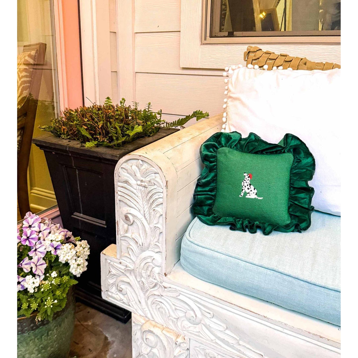 Green Dalmatian needlepoint pillow with ruffled edges on white carved couch outdoors