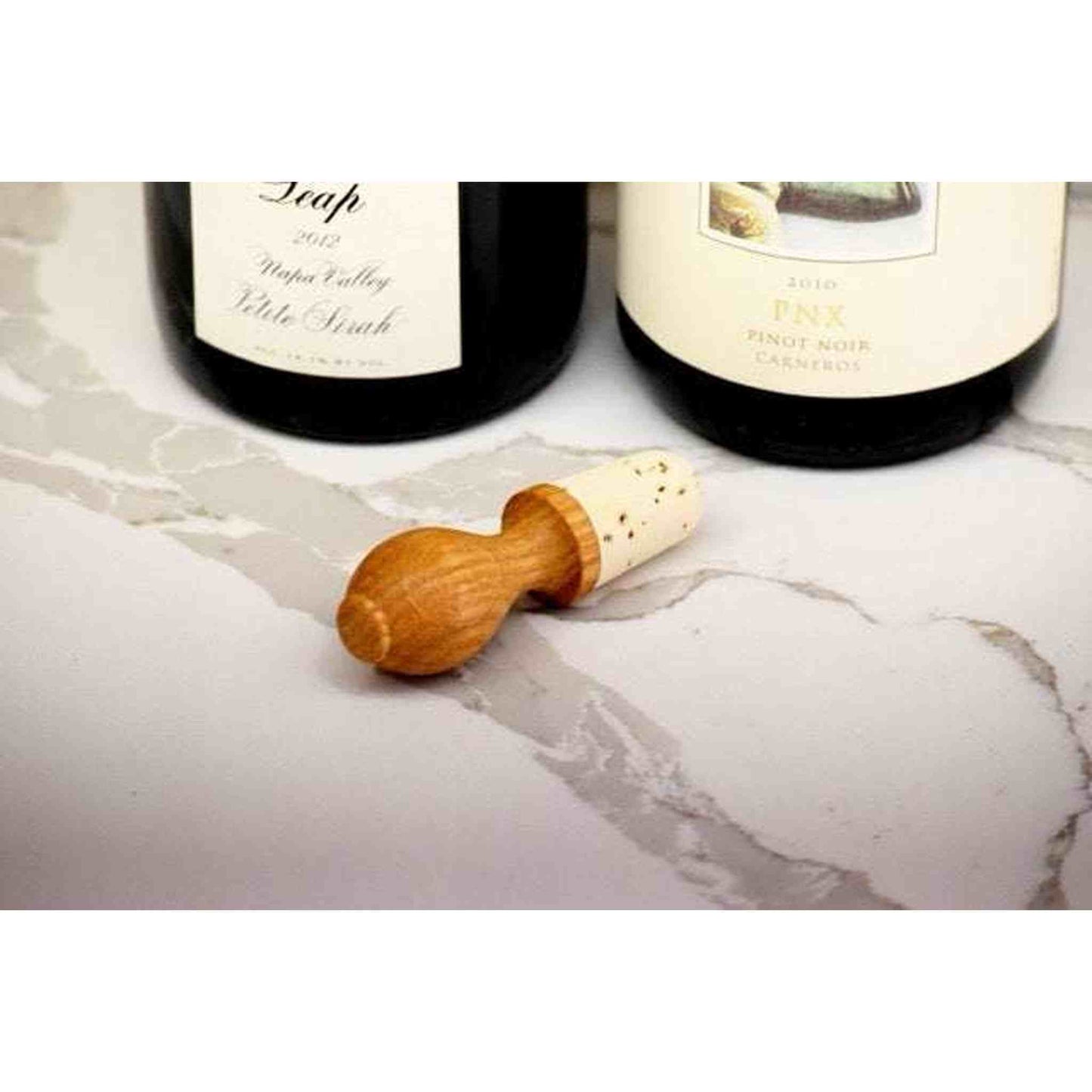 Oak wine stopper made from natural cork and FSC oak, 3 inches tall, shown beside wine bottles