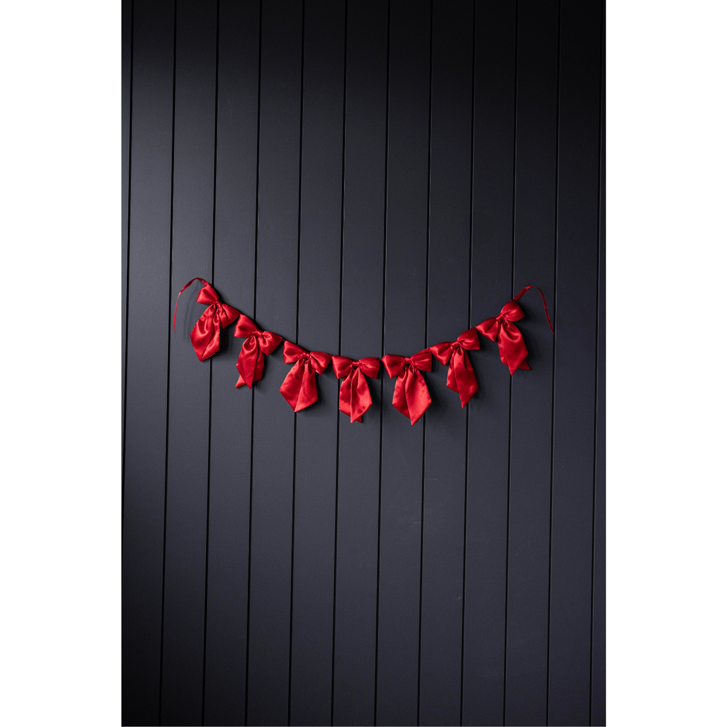 Red Satin Bow Garland with seven satin bows hanging on a dark wall background