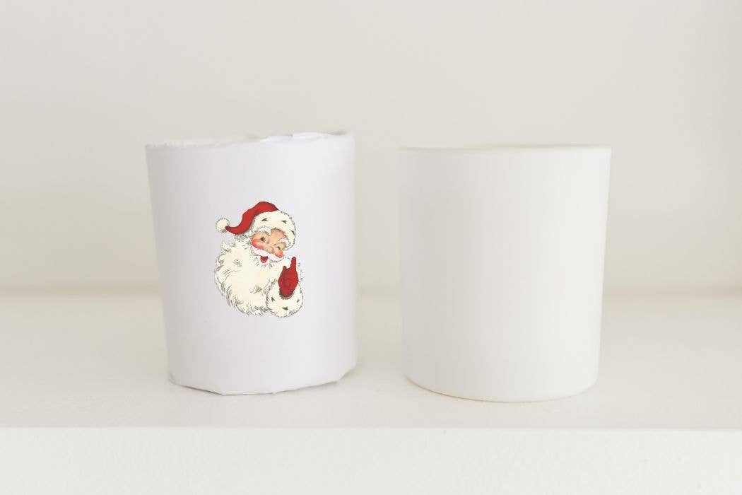 10oz Christmas candle with Santa illustration wrapped in white paper with holiday scent of Fraser Fir in white glass vessel