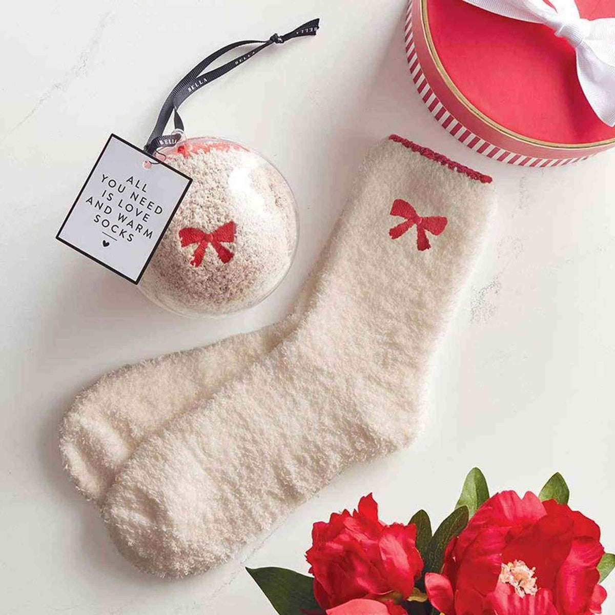 
                  
                    Blush cozy socks with red bow detail made from soft polyester displayed with gift packaging and red flowers
                  
                