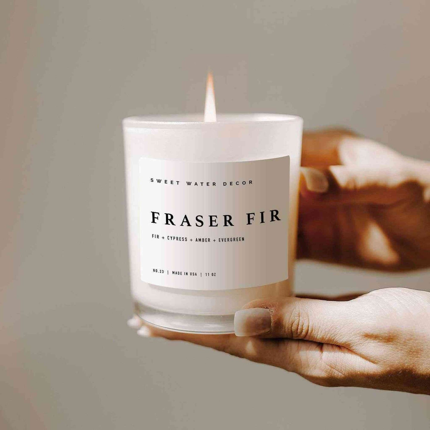 Hand holding lit Fraser Fir soy candle in white glass jar with minimalist label