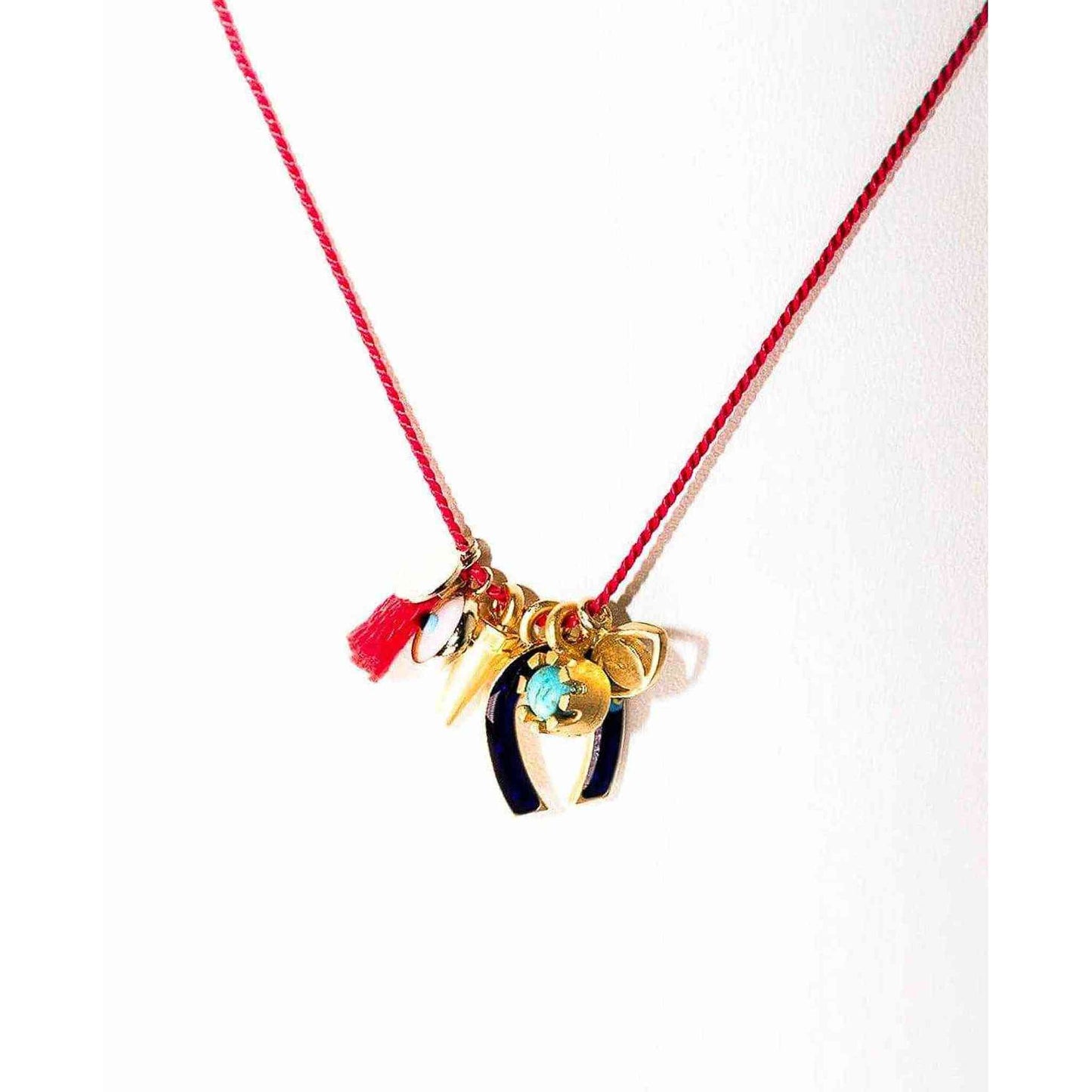 All The Luck Charm Necklace with red silk string, gold clasps, ceramic evil eye, gold spike, enamel horseshoe, turquoise gem, and red tassel charms