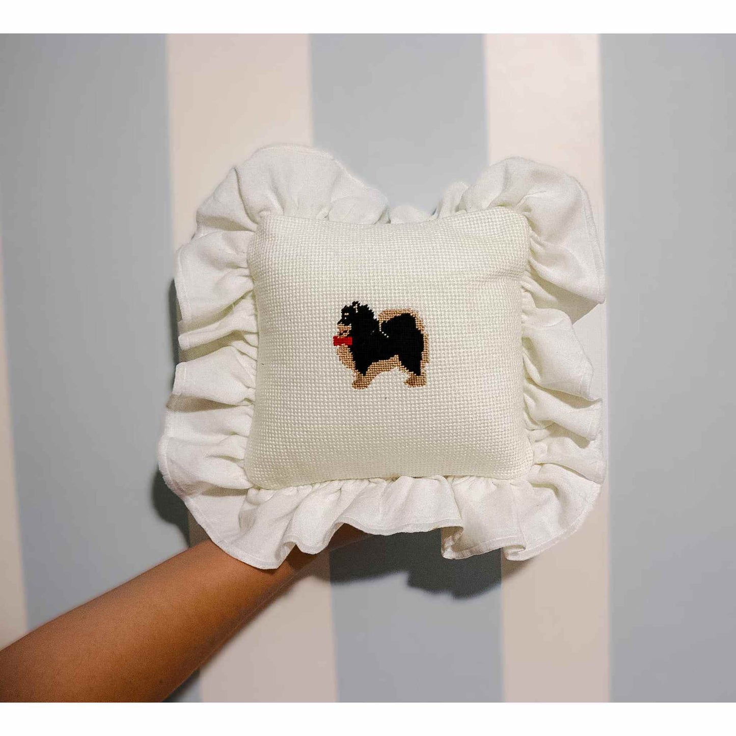 Pomeranian needlepoint pillow with ruffled white edges on a hand-held beige background