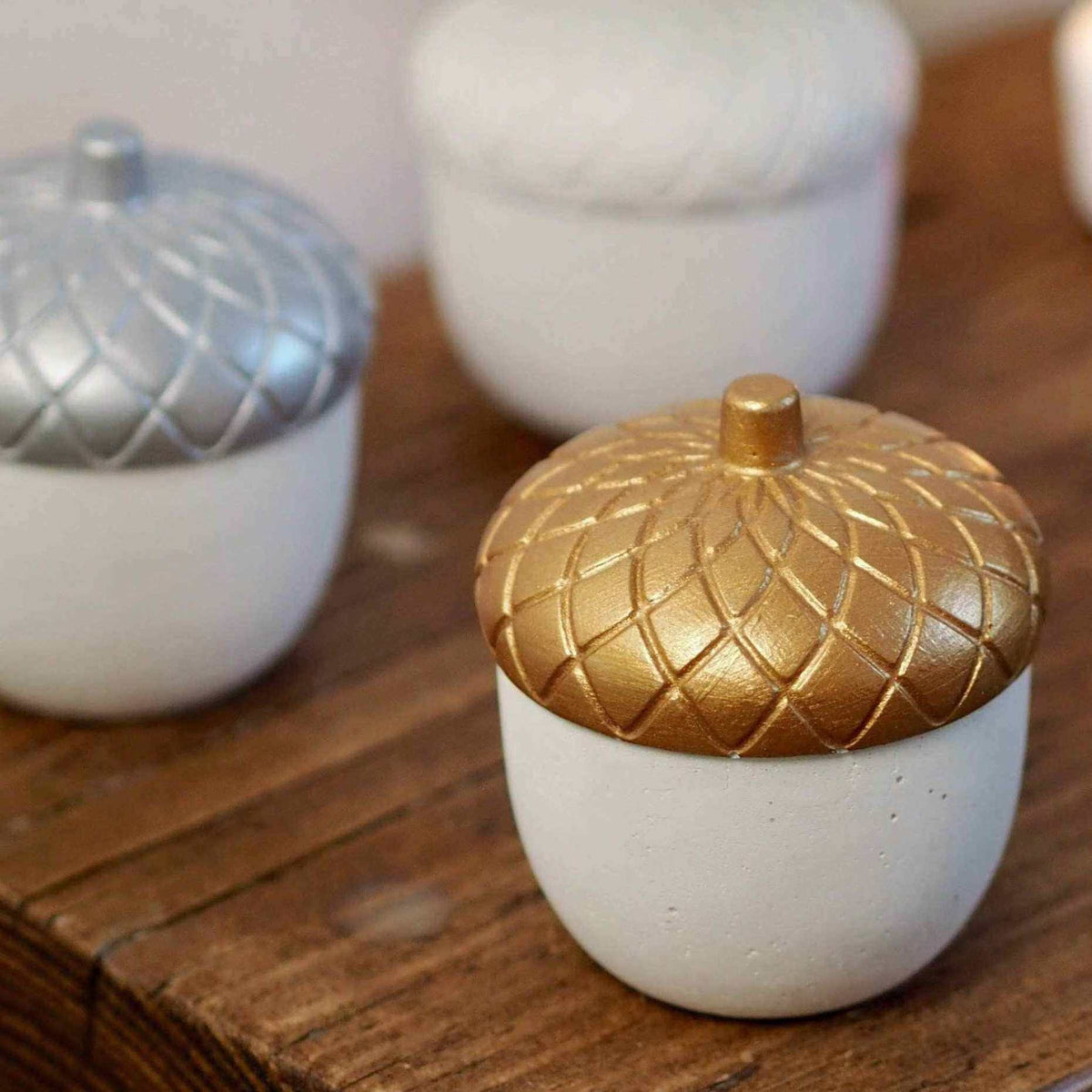 
                  
                    Handmade concrete acorn paperweight with solid white base and gold top on wooden surface
                  
                