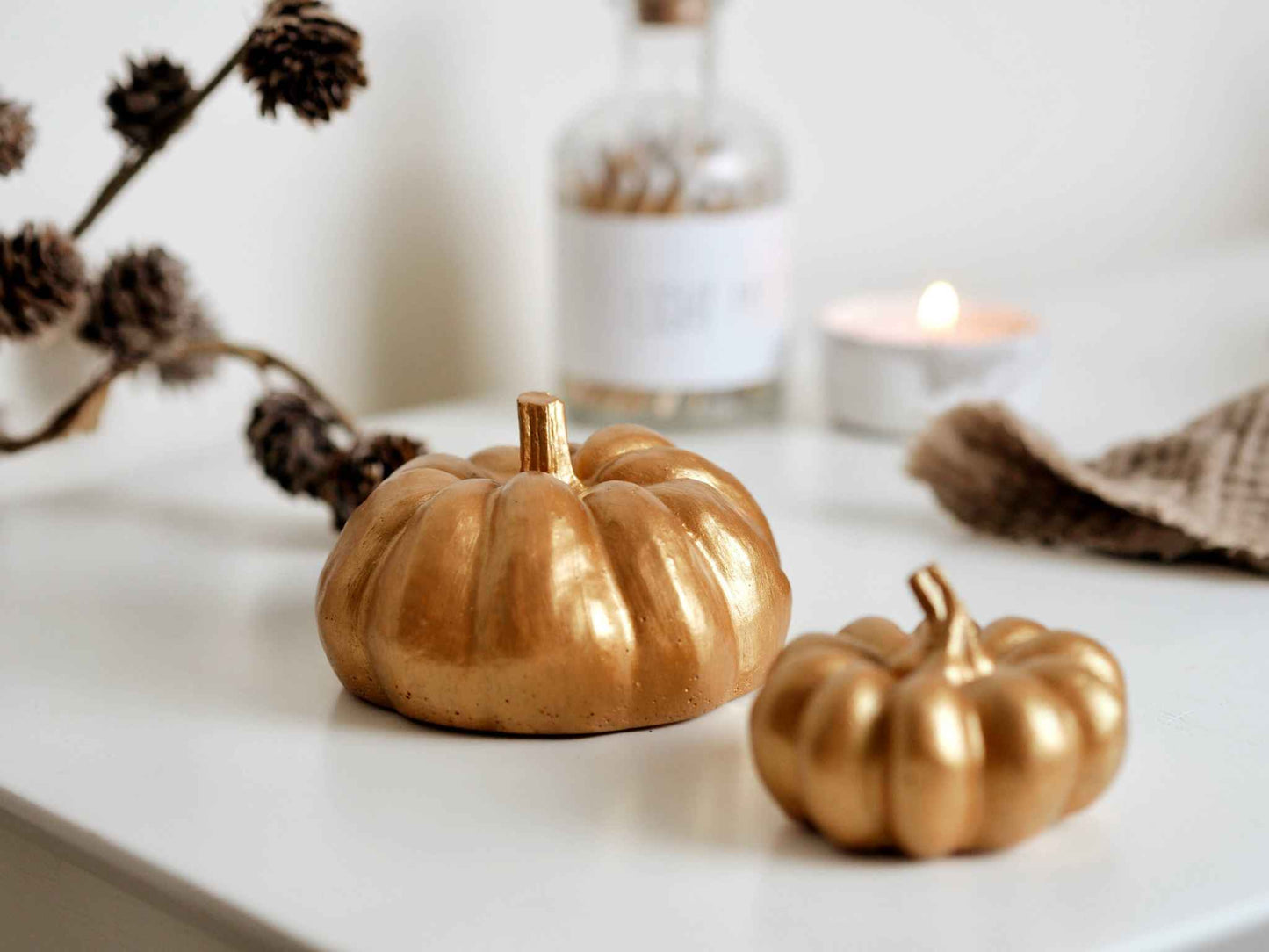 small gold concrete pumpkin decoration on white surface with blurred autumn decor background