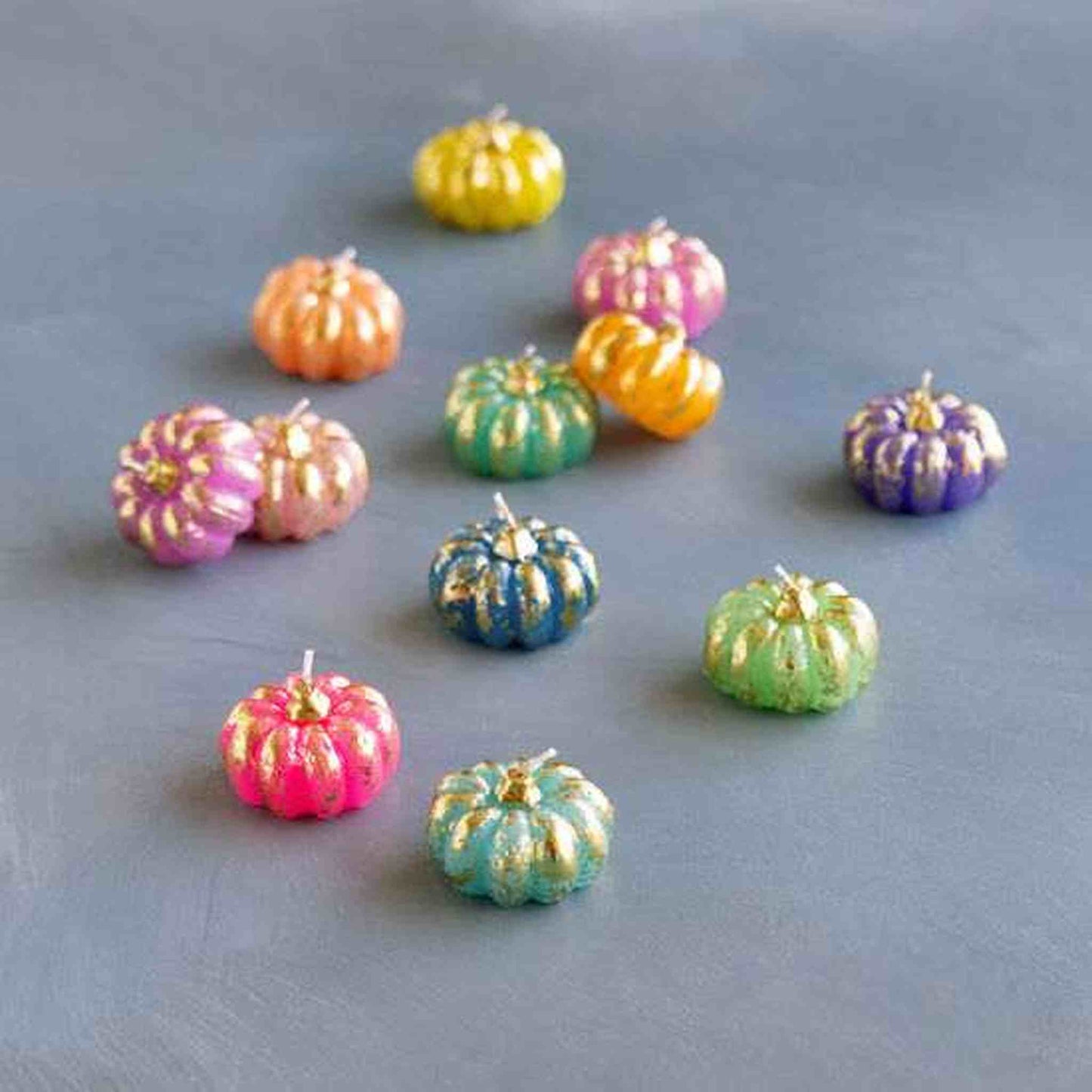 Set of 6 colorful rainbow pumpkin tea lights with golden gild accents on gray surface