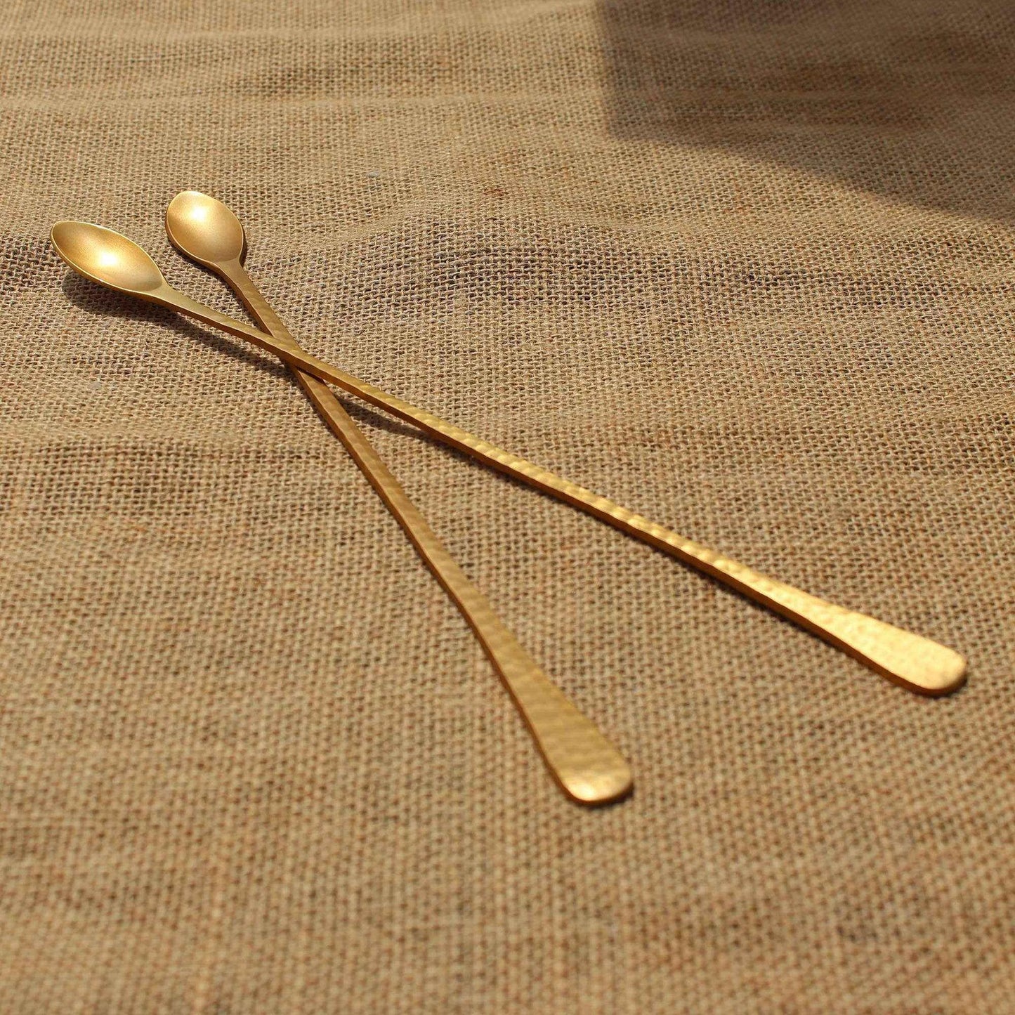 Set of two pebbled long brass bar spoons with hammered texture and matte gold finish on burlap background